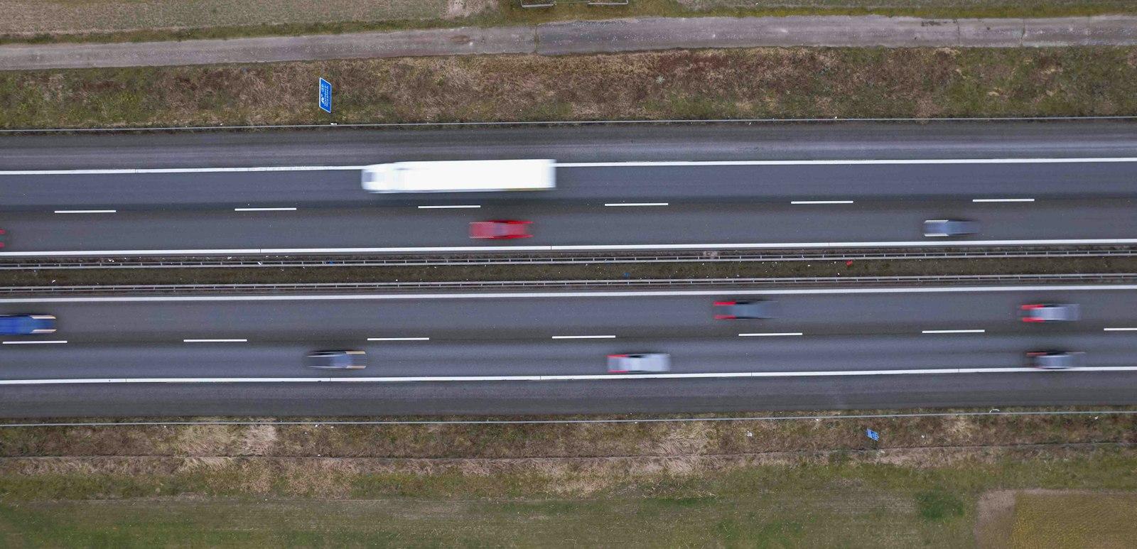 Vue aérienne d'une autoroute à deux fois deux voies, véhicules en mouvement et bas-côtés herbeux.